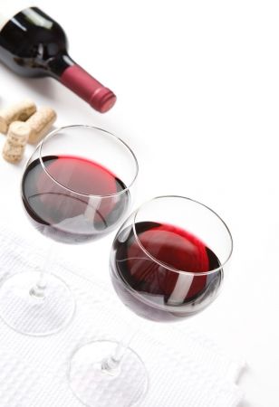 Due bicchieri di vino rosso con dietro dei tappi e una bottiglia stesa